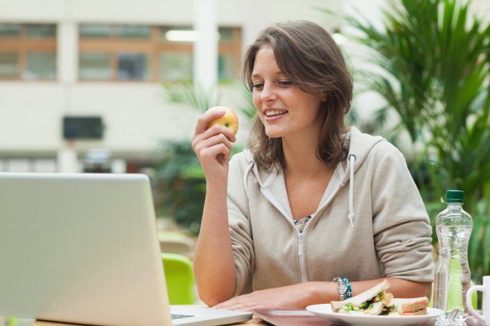 Young woman using laptop while eating apple